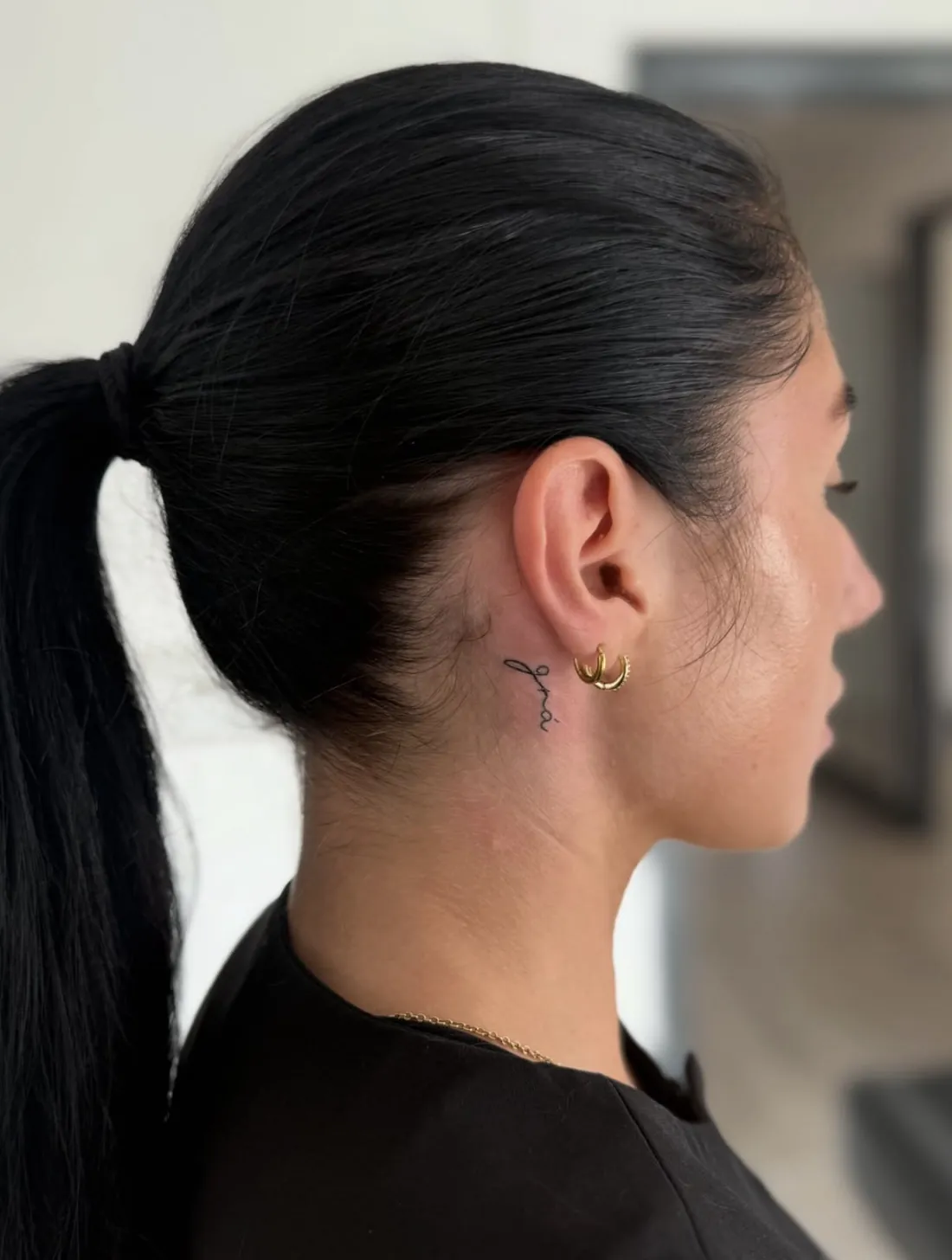 Tiny script tattoo reading grá behind the ear