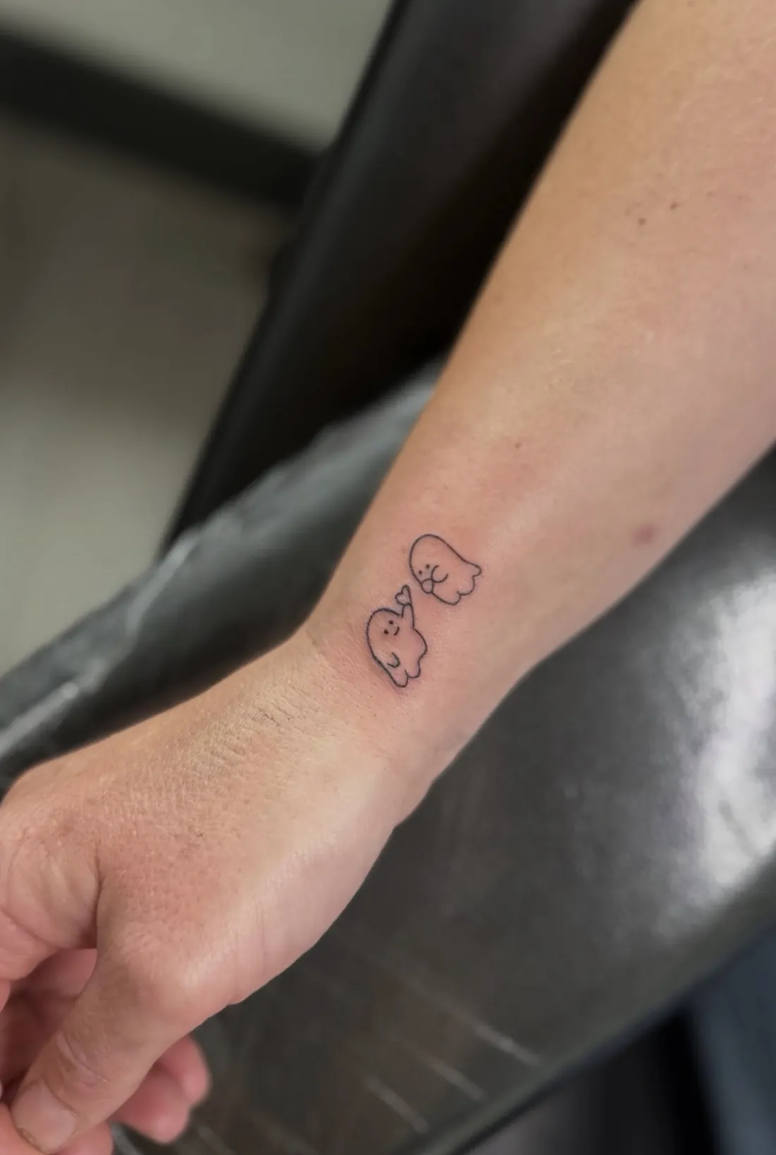 Two tiny cartoon ghosts sharing a heart on the wrist