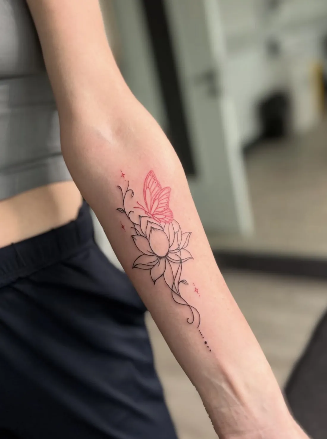 Fine line lotus with a red butterfly and sparkles on the forearm