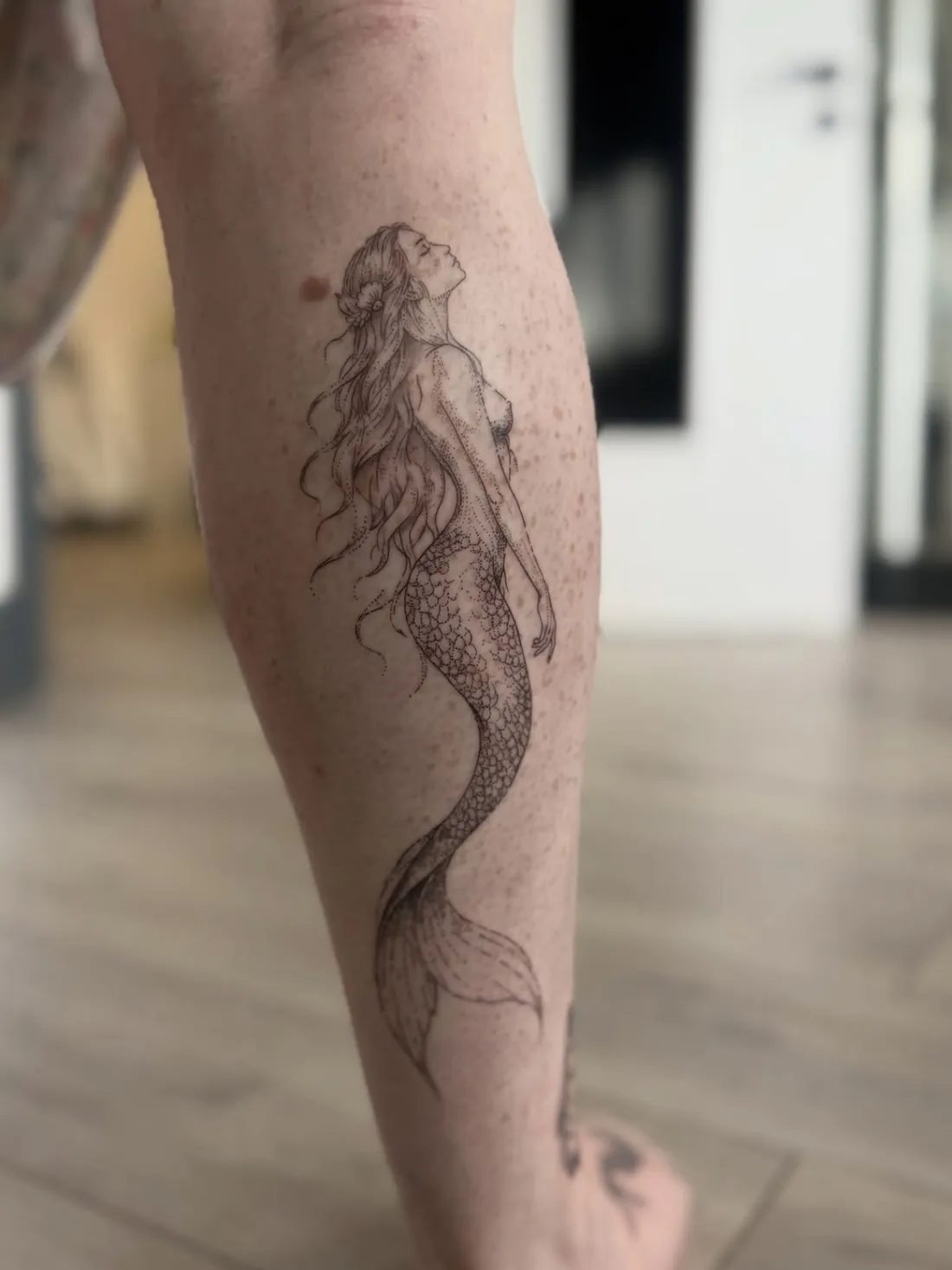 Dotwork mermaid with flowing hair and a scaled tail on the calf