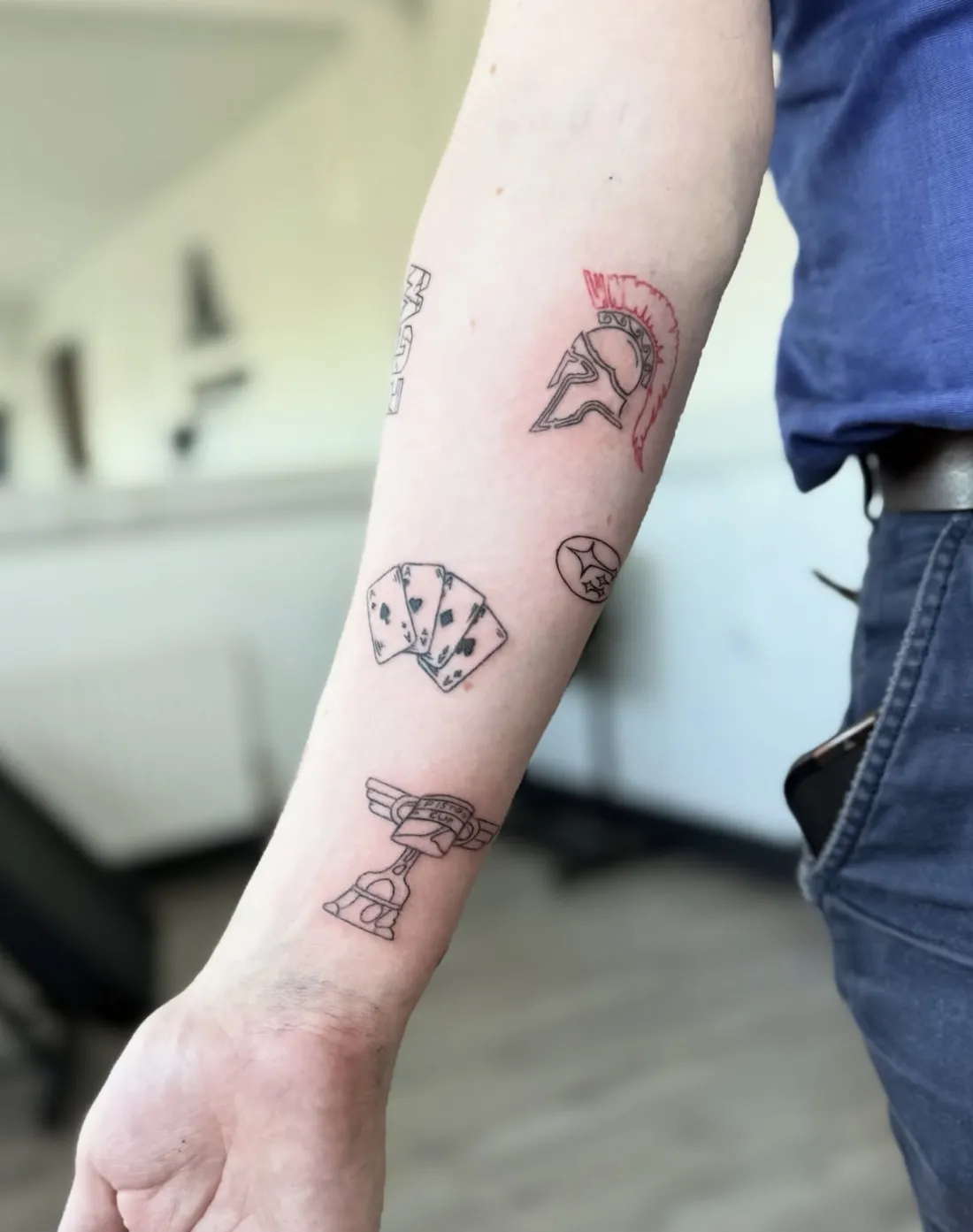 Patchwork forearm with a red-crested helmet, playing cards and small line tattoos