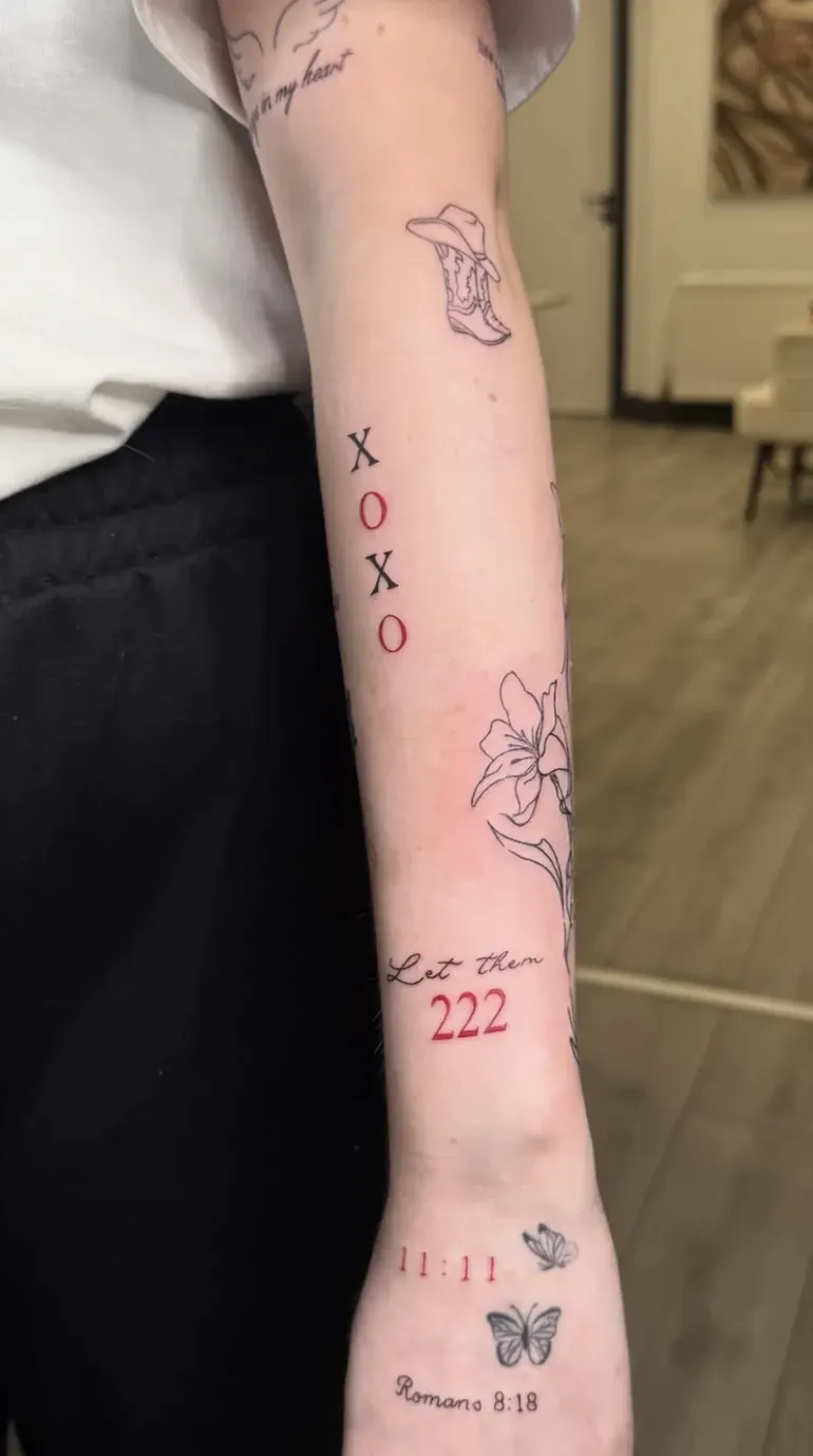 Patchwork forearm of small black and red tattoos including XOXO, 222 and butterflies