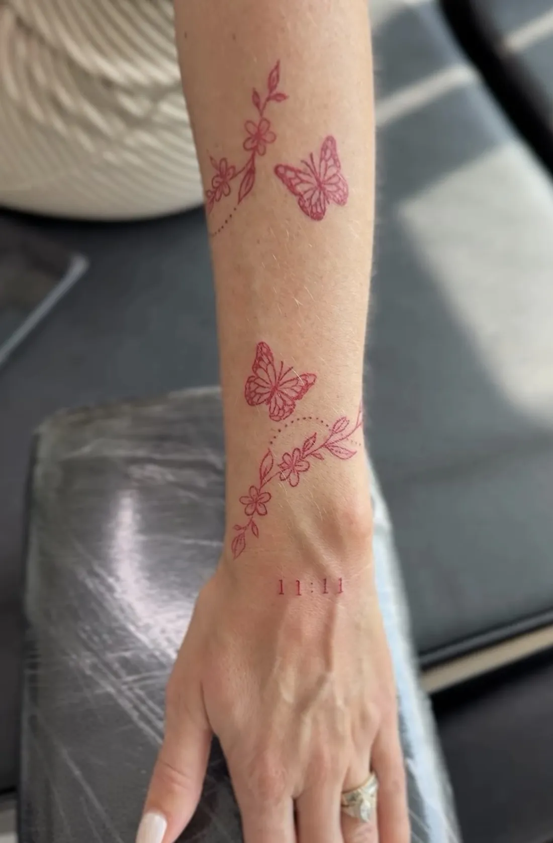 Red ink butterflies and flowering vines wrapping the forearm, with 11:11 at the wrist