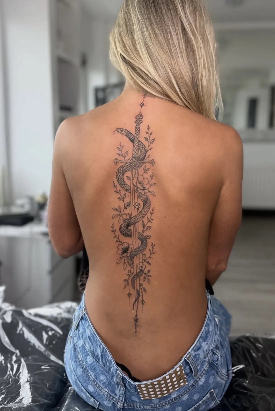 Fine line snake coiled around an ornate sword with florals down the spine